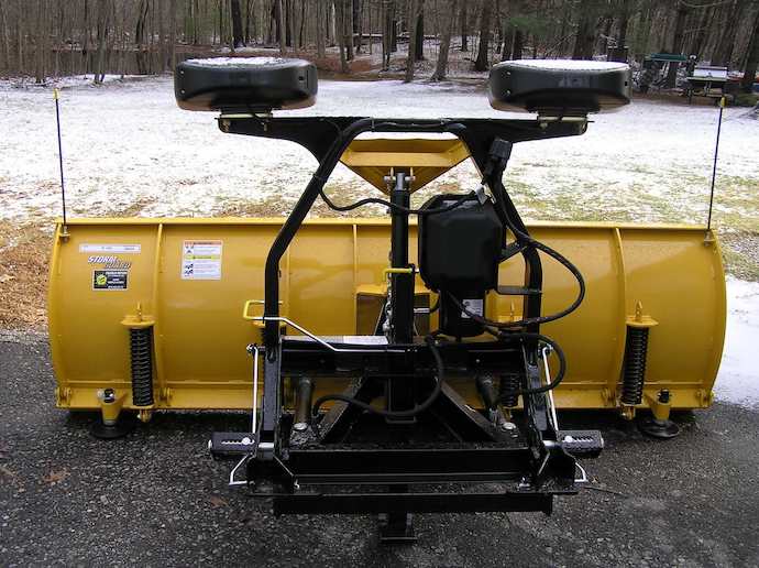 Yellow snow plow in a driveway with snow in the background